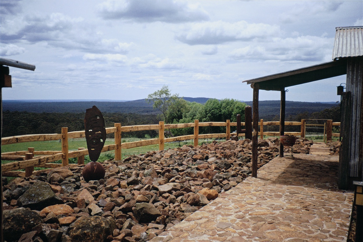 Post and rail fence above a basalt rock garden, with a covered walkway and long views across paddocks