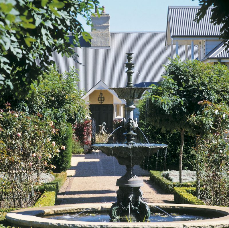 Tiered fountain on a gravel axis between clipped box hedges, close to the house at a Southern Highlands country estate