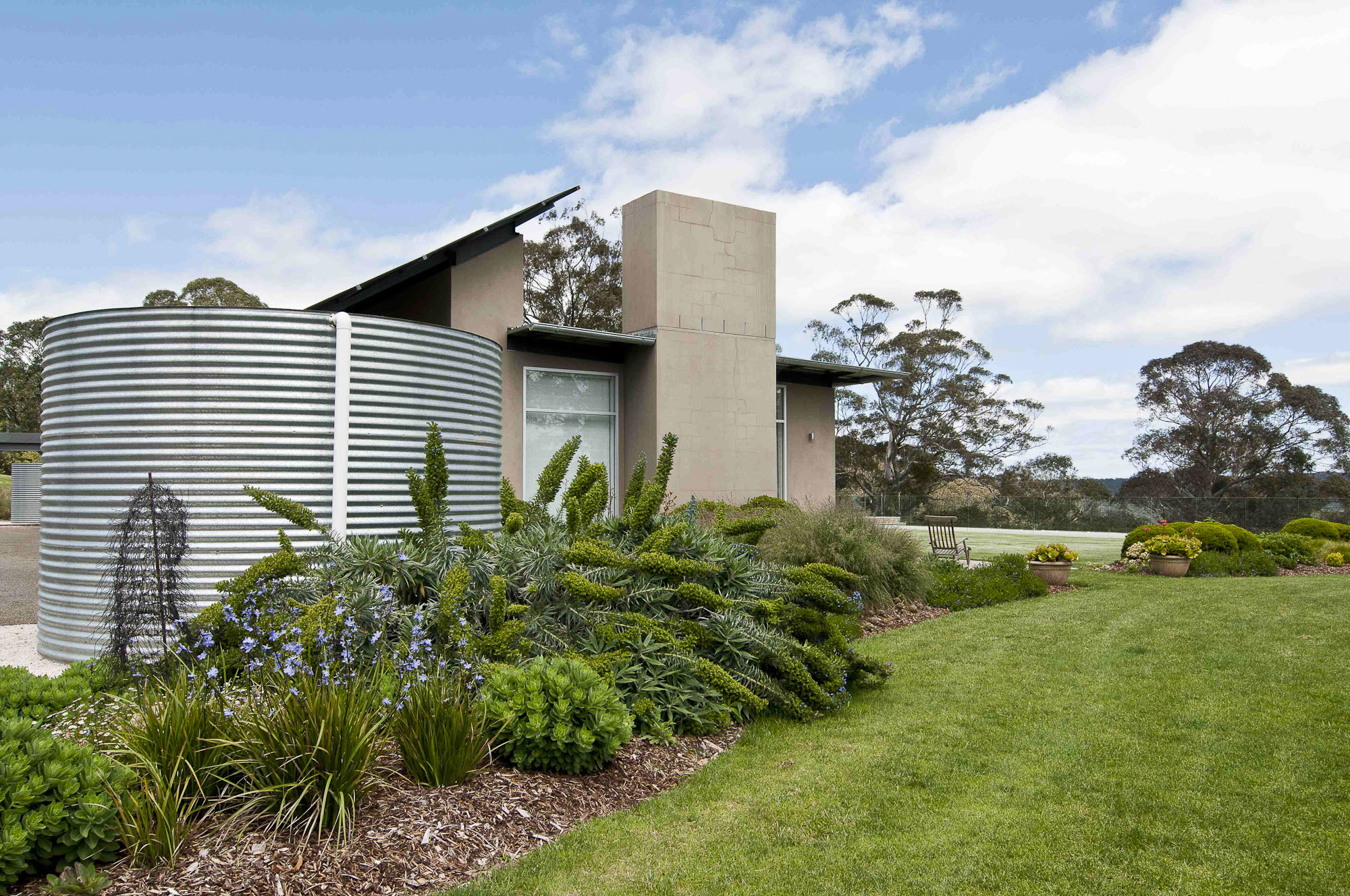Corrugated water tank beside a contemporary country house, with native planting and mown lawn