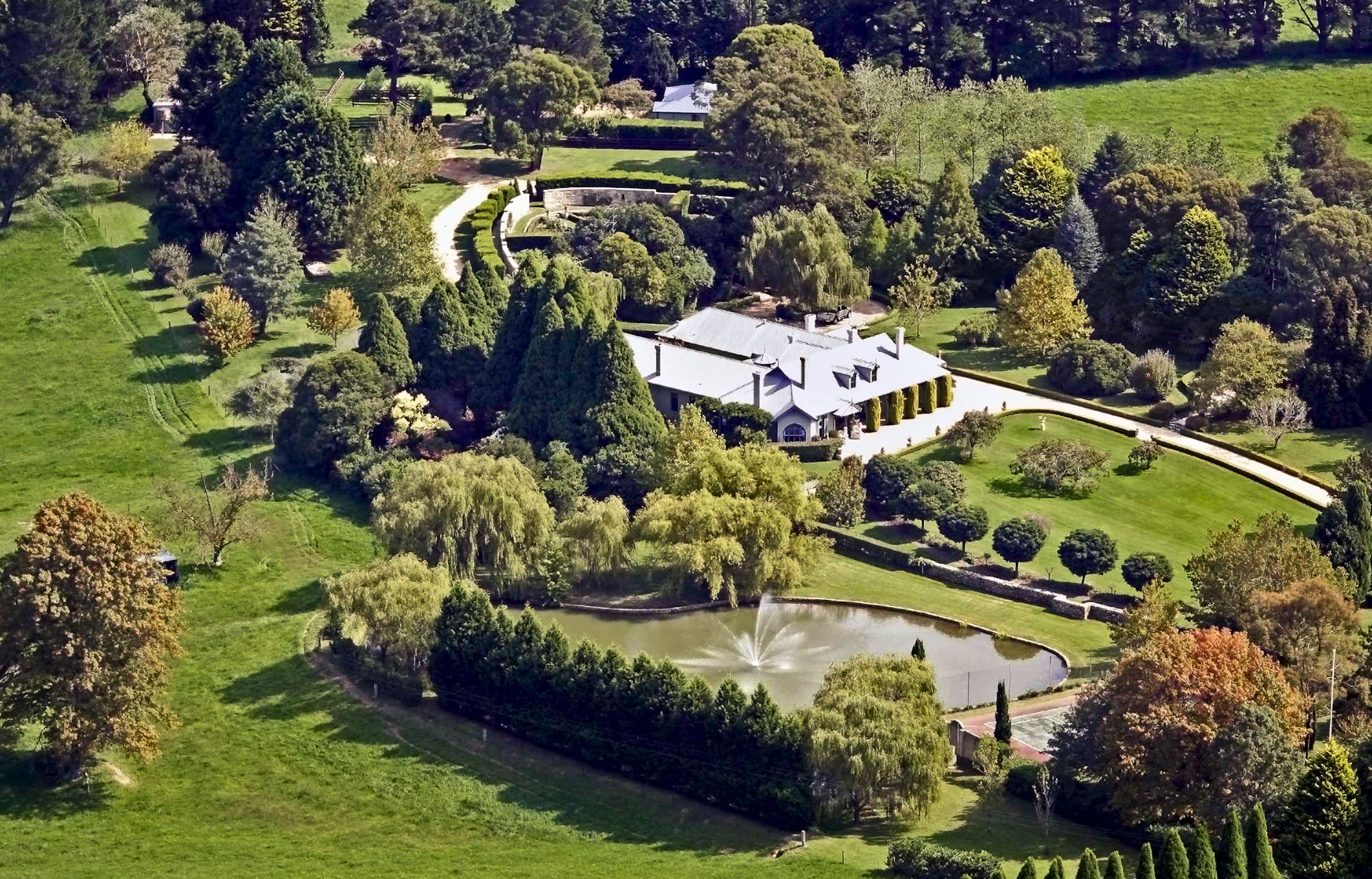 Aerial view of a country house garden with a lake, clipped hedges and belts of trees set among open paddocks
