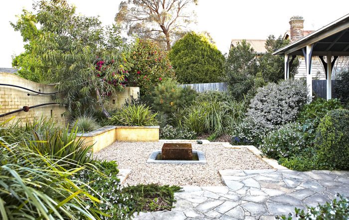 Gravel courtyard and stone paving with low planting beside a weatherboard house in the Southern Highlands