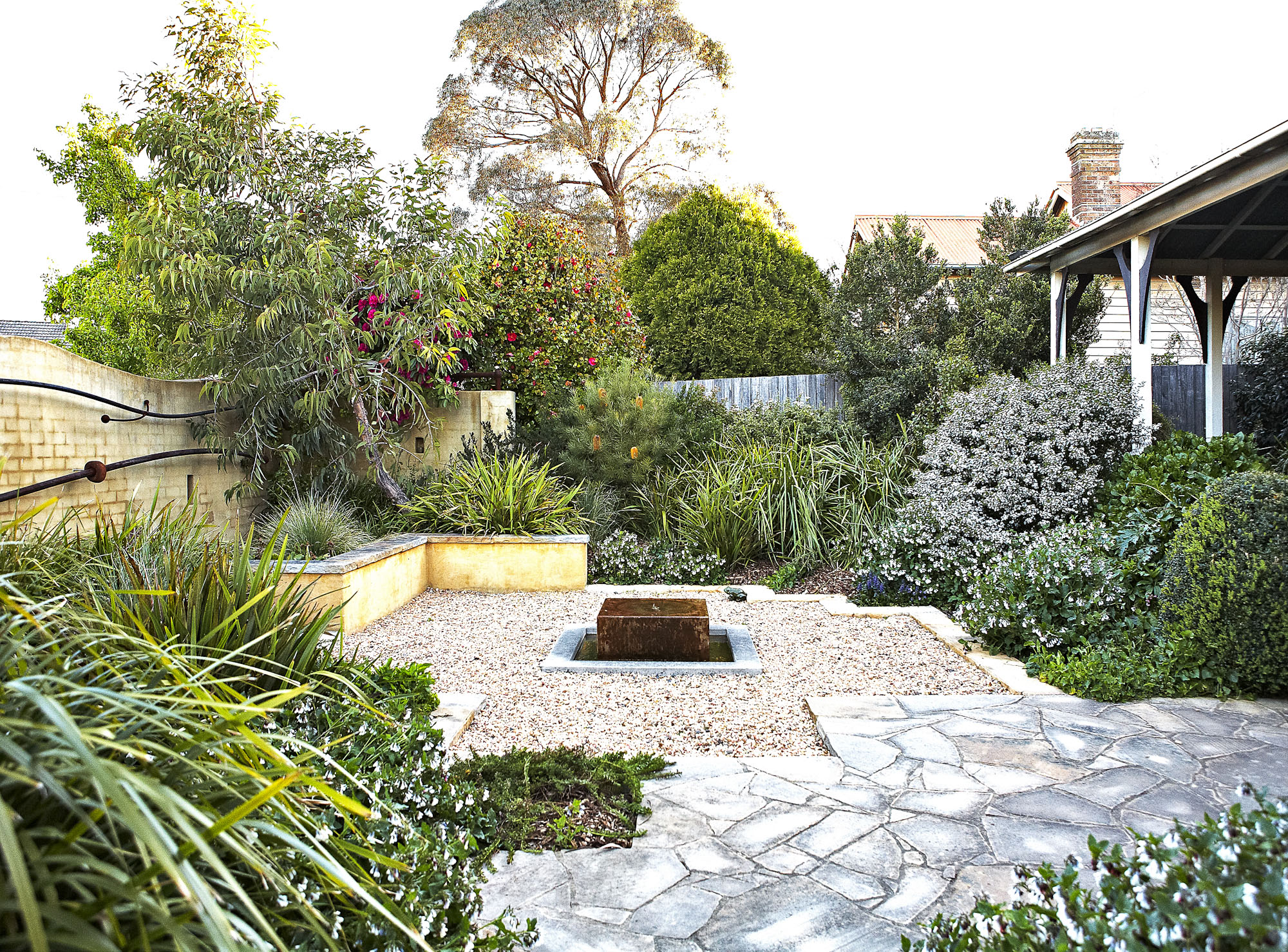 Gravel courtyard and stone paving with low planting beside a weatherboard house in the Southern Highlands